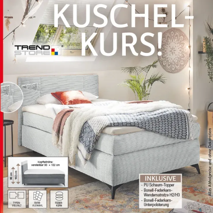 Gemütliche Schlafzimmerszene mit hellgrauem Boxspringbett von Trendstore, kuscheligen Decken und stimmungsvoller Beleuchtung, präsentiert unter dem Angebotstitel „Kuschelkurs“.